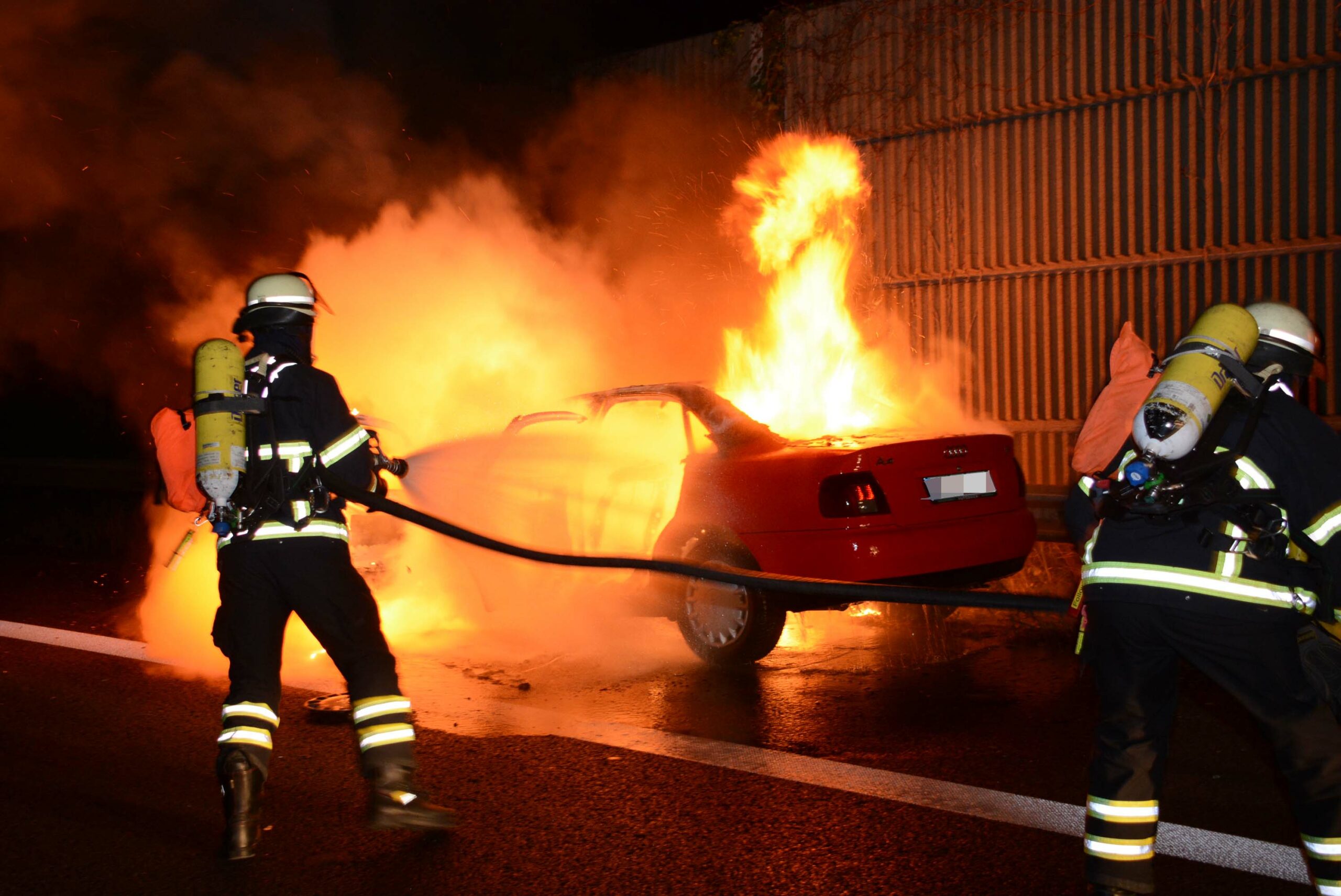 Feuerwehrleute löschen den brennenden Audi.