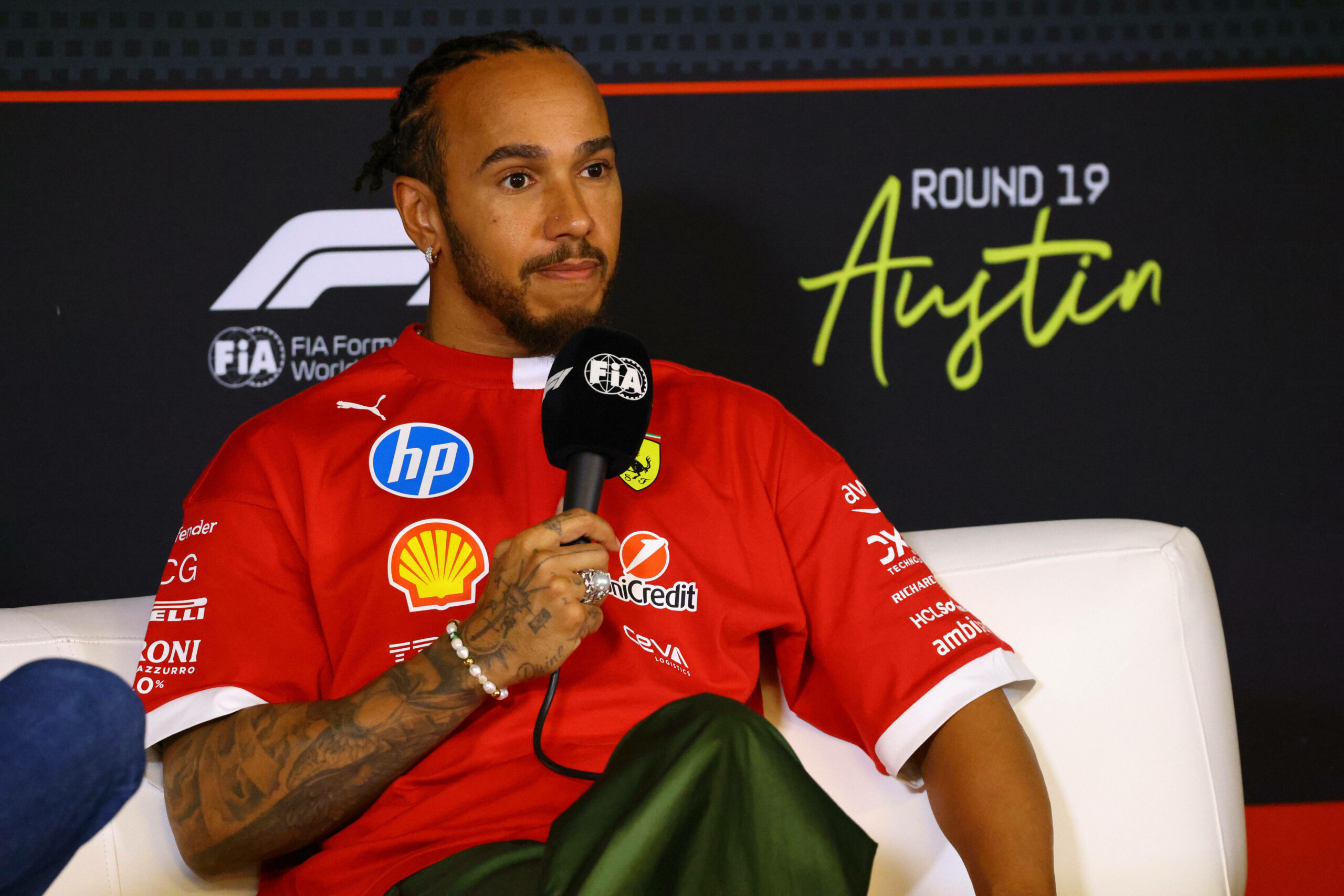 Ein sichtlich genervter Lewis Hamilton im Ferrari-Shirt auf der Pressekonferenz mit einem Mikro in der Hand
