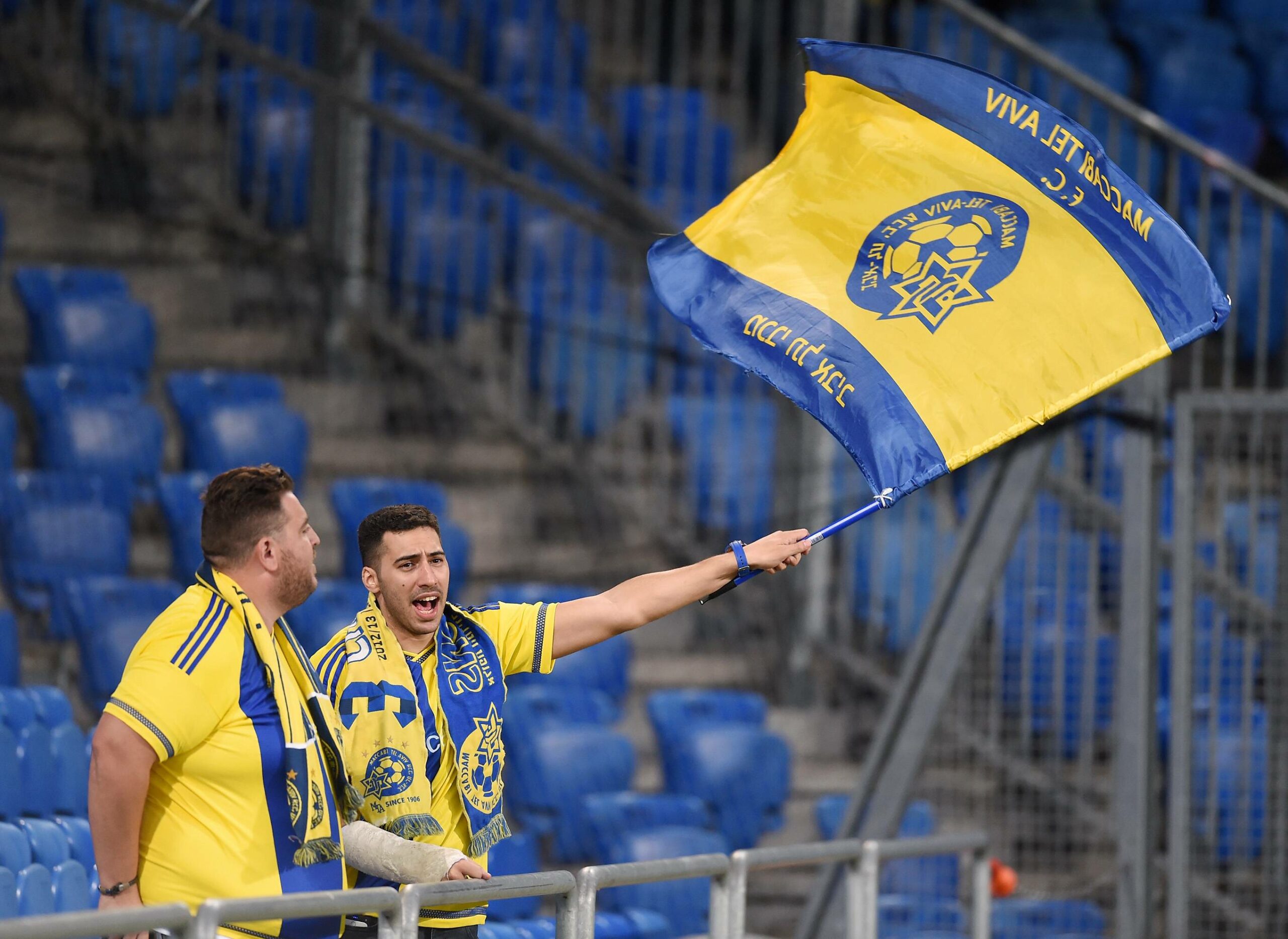 Zwei Maccabi Tel Aviv-Fans unterstützen in Trikots und Schal mit einer Flagge ihr Team