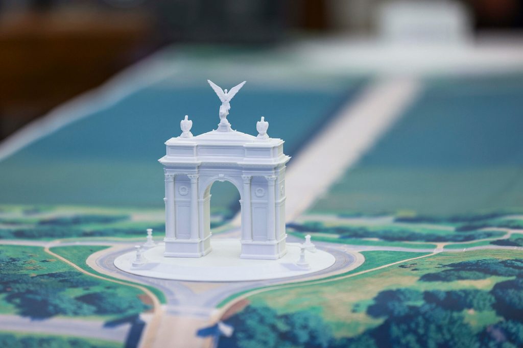 Ein weißes Modell des Triumphbogens. Mit zahlreichen Details, wie Säulen an den Ecken. Oben drauf in der Mitte, thront ein Engel mit ausgebreiteten Flügeln. Links und rechts von dem Engel befindet sich jeweils ein Adler.