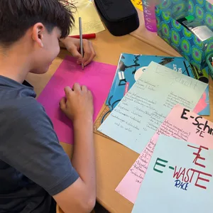 Zwei Schüler sitzen an einem Tisch und bemalen bunte Plakate.