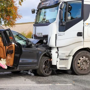 Ein schwarzer Porsche-SUV steht mit der Frontpartie in einen weißen Lastwagen gedrückt.