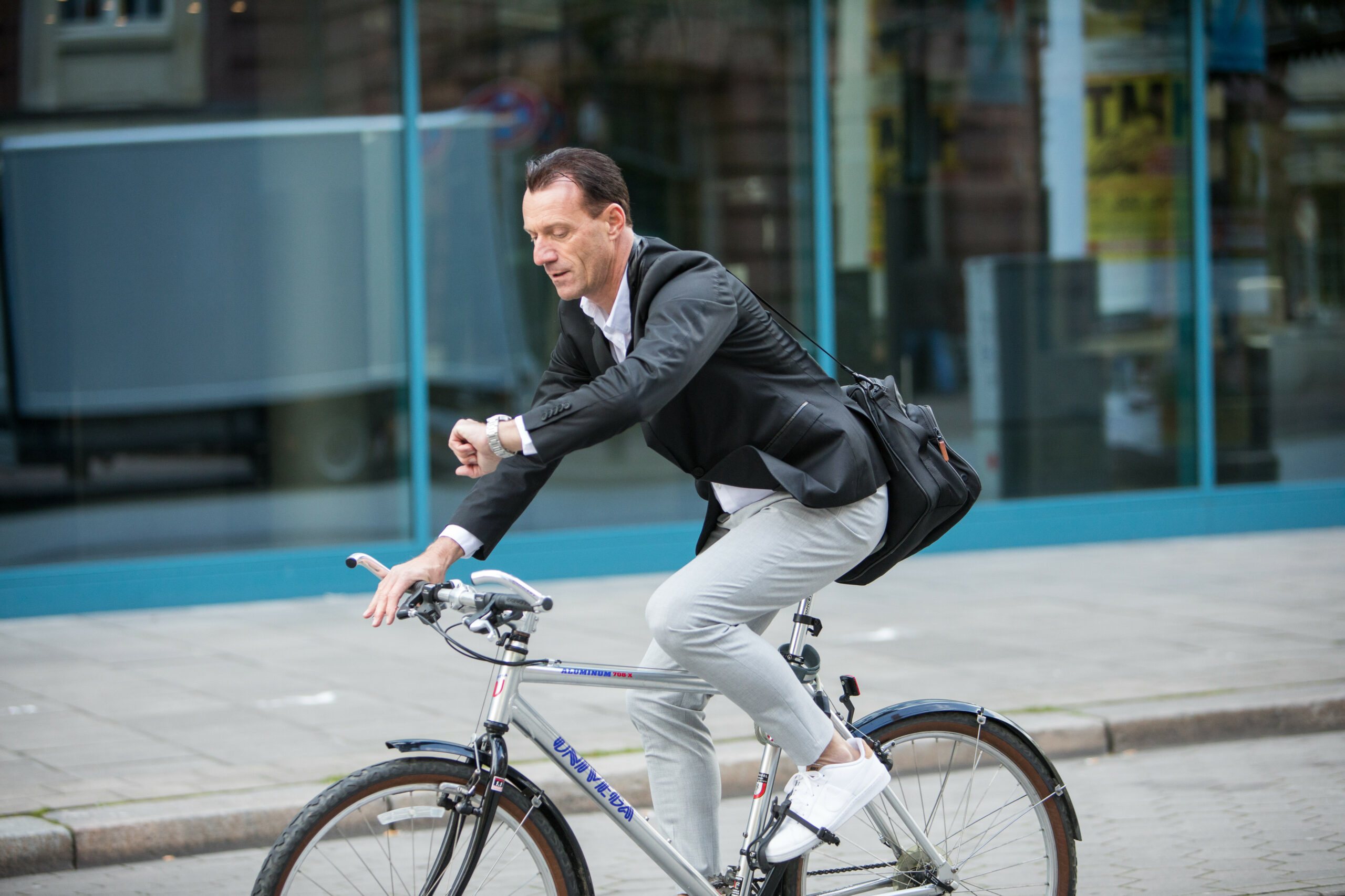 Mann fährt mit Fahrrad durch Stadt und guckt auf Uhr.