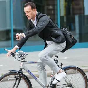 Mann fährt mit Fahrrad durch Stadt und guckt auf Uhr.