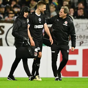 St. Pauli-Verteidiger Karol Mets wird von zwei St. Pauli-Betreuern vom Spielfeld begleitet