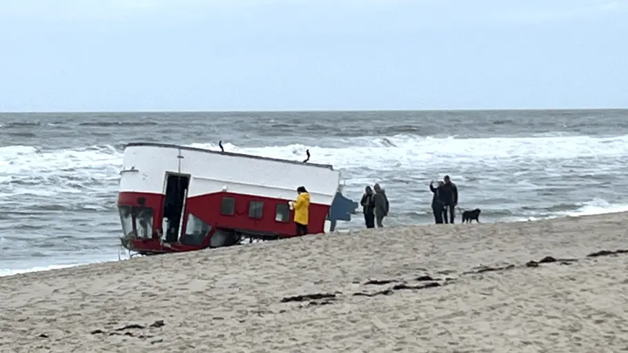 Das Boot liegt kopf über am Strand; Menschen sammeln sich drum herum an.
