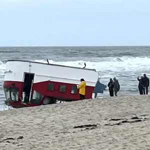 Das Boot liegt kopf über am Strand; Menschen sammeln sich drum herum an.