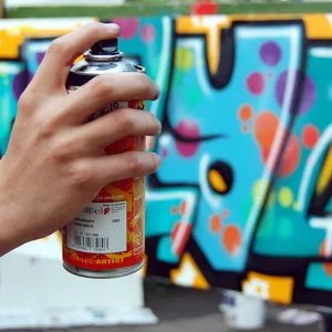 Eine Hand hält ein Grafitti-Spraydose vor einer besprühten Wand.