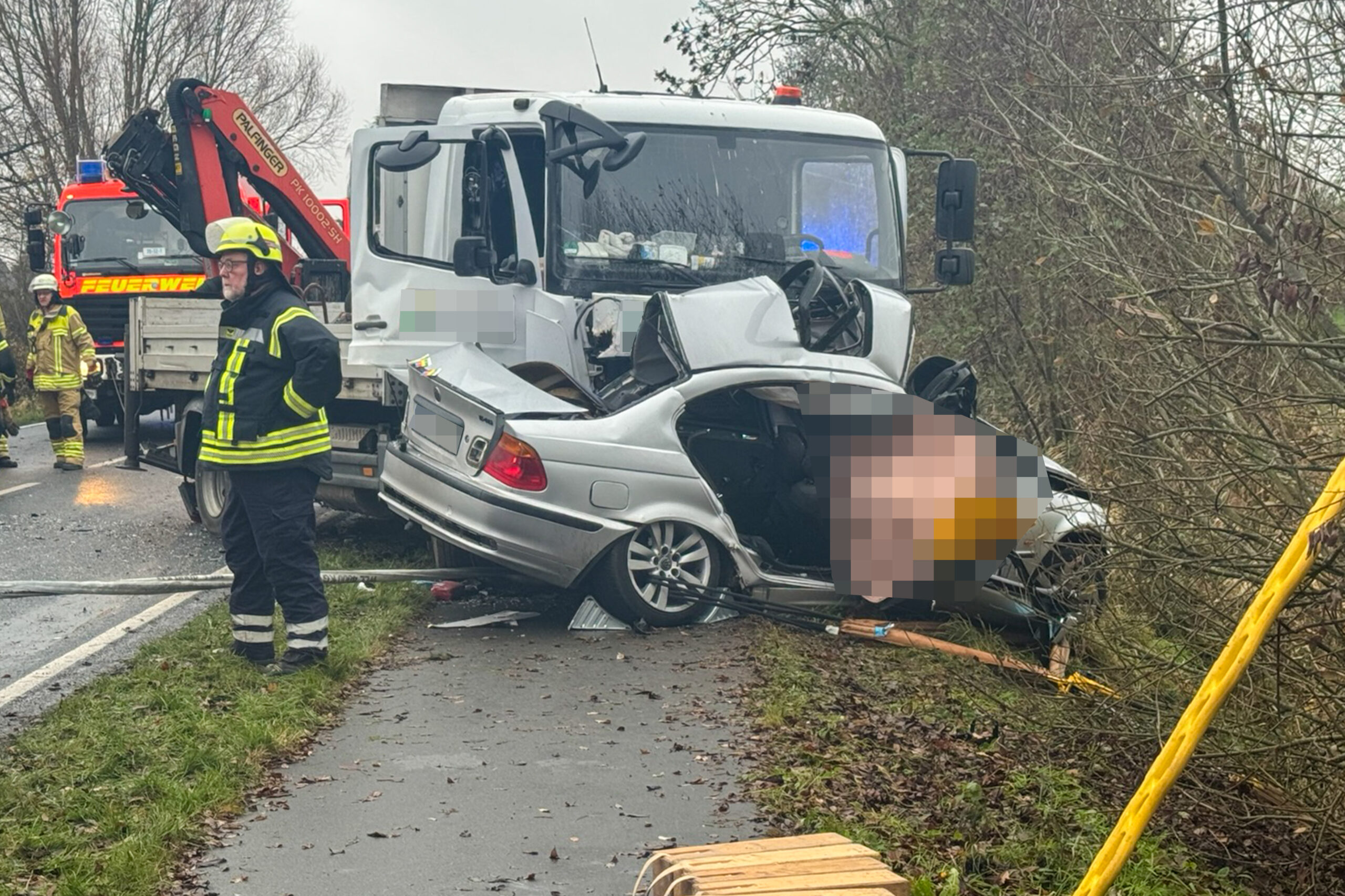 Ein Lkw und ein BMW stehen am Straßenrand. Der BMW liegt schräg über einer Böschung.