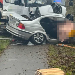 Ein Lkw und ein BMW stehen am Straßenrand. Der BMW liegt schräg über einer Böschung.
