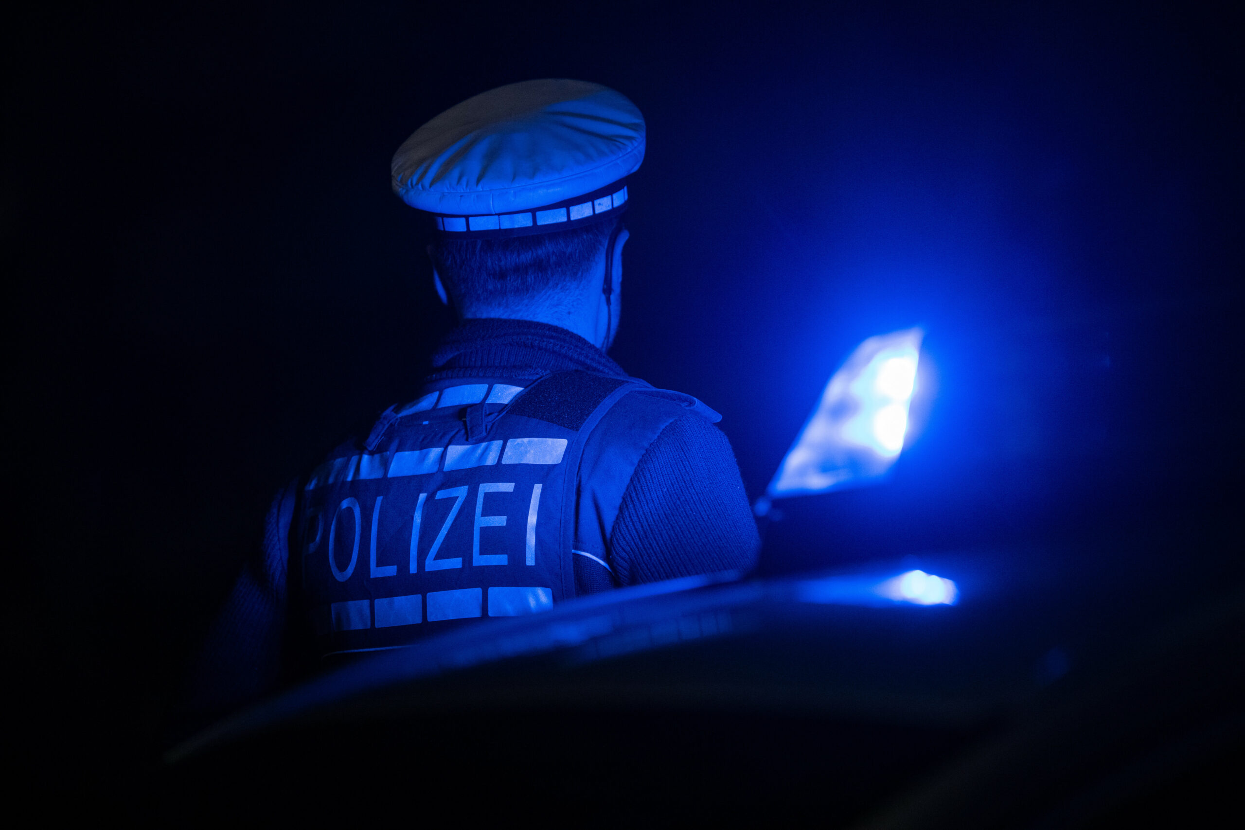 Ein Polizist steht neben einem Polizeifahrzeug.