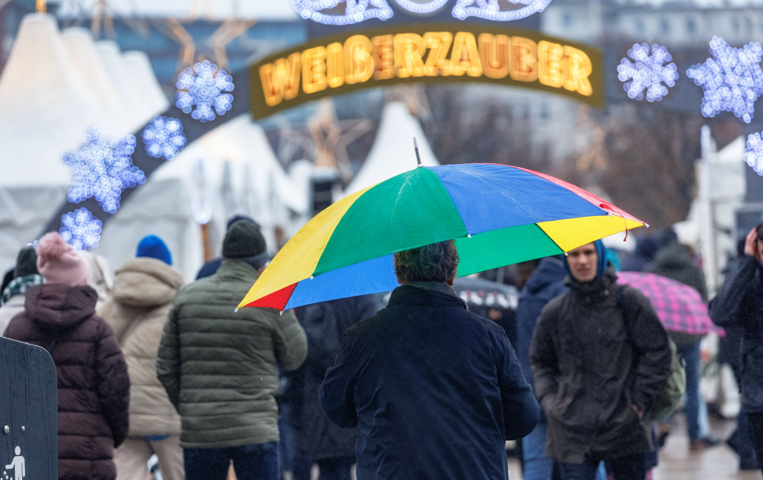 Ein Mann geht im Nieselregen mit seinem Schirm über einen Weihnachtsmarkt.
