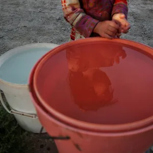 Ein kleines Kind steht vor einem Eimer Wasser.