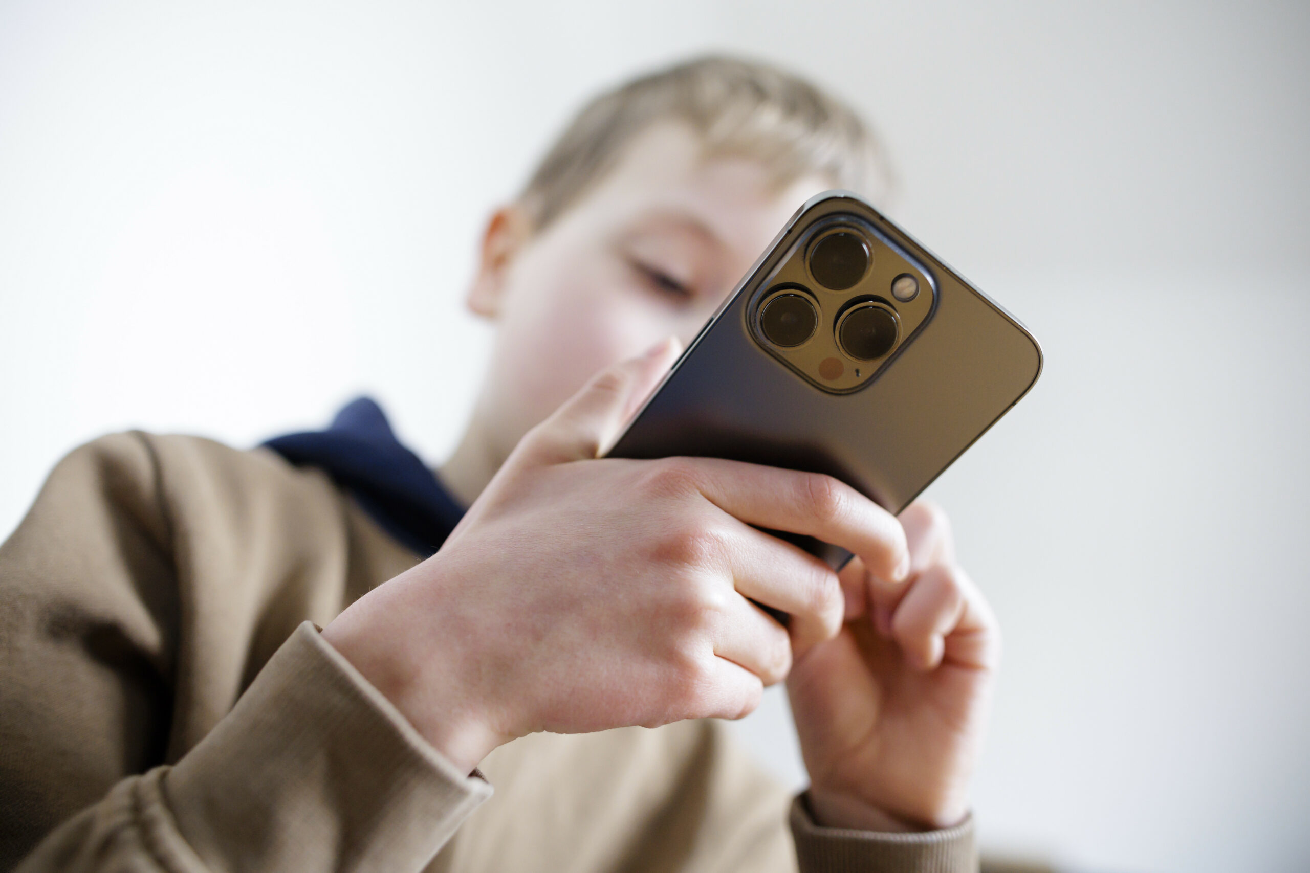 Ein Kind im braunen Pullover schaut auf ein Handy.