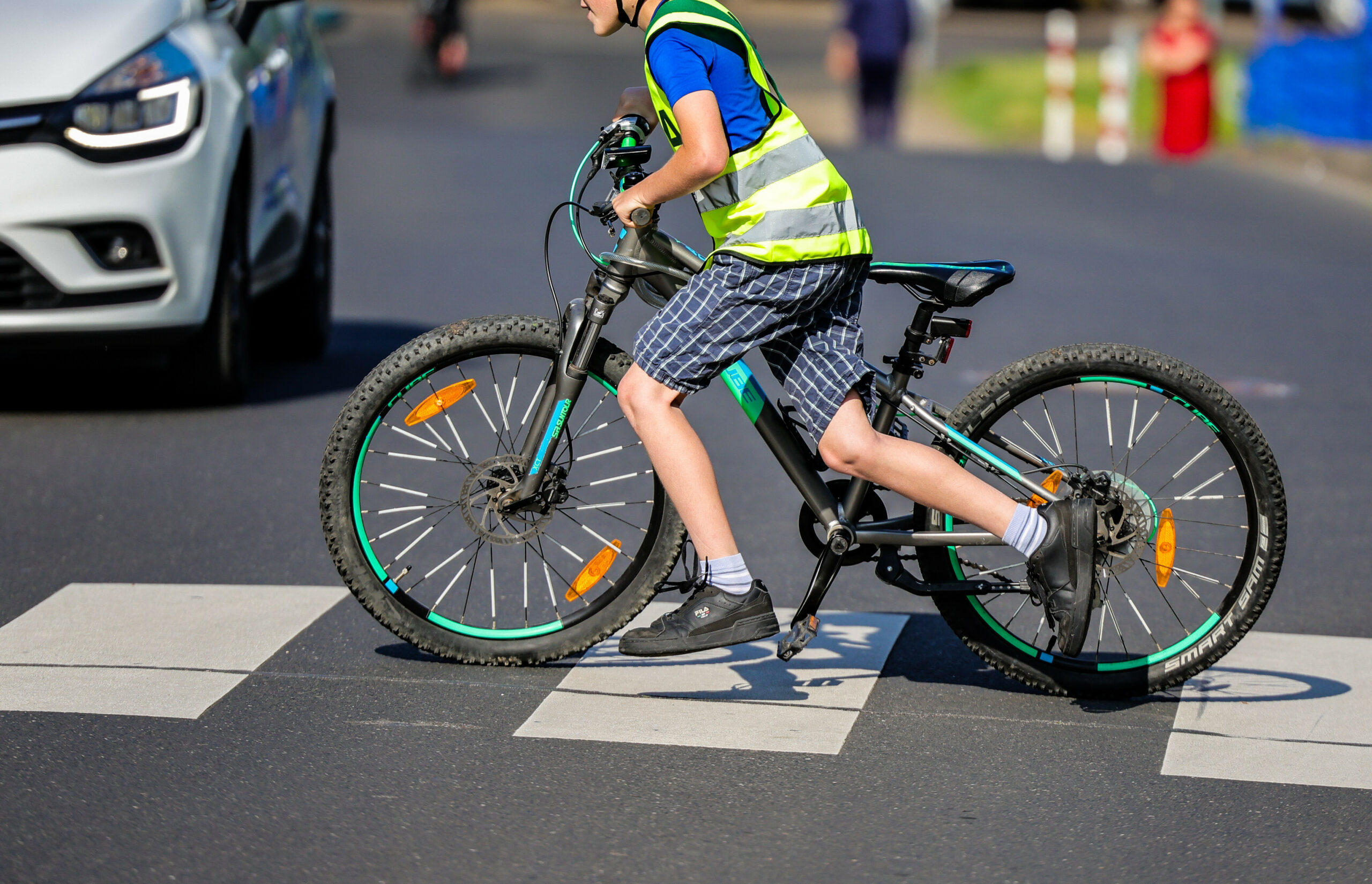 Ein Kind mit Warnweste schiebt sein Fahrrad über einen Zebrastreifen.