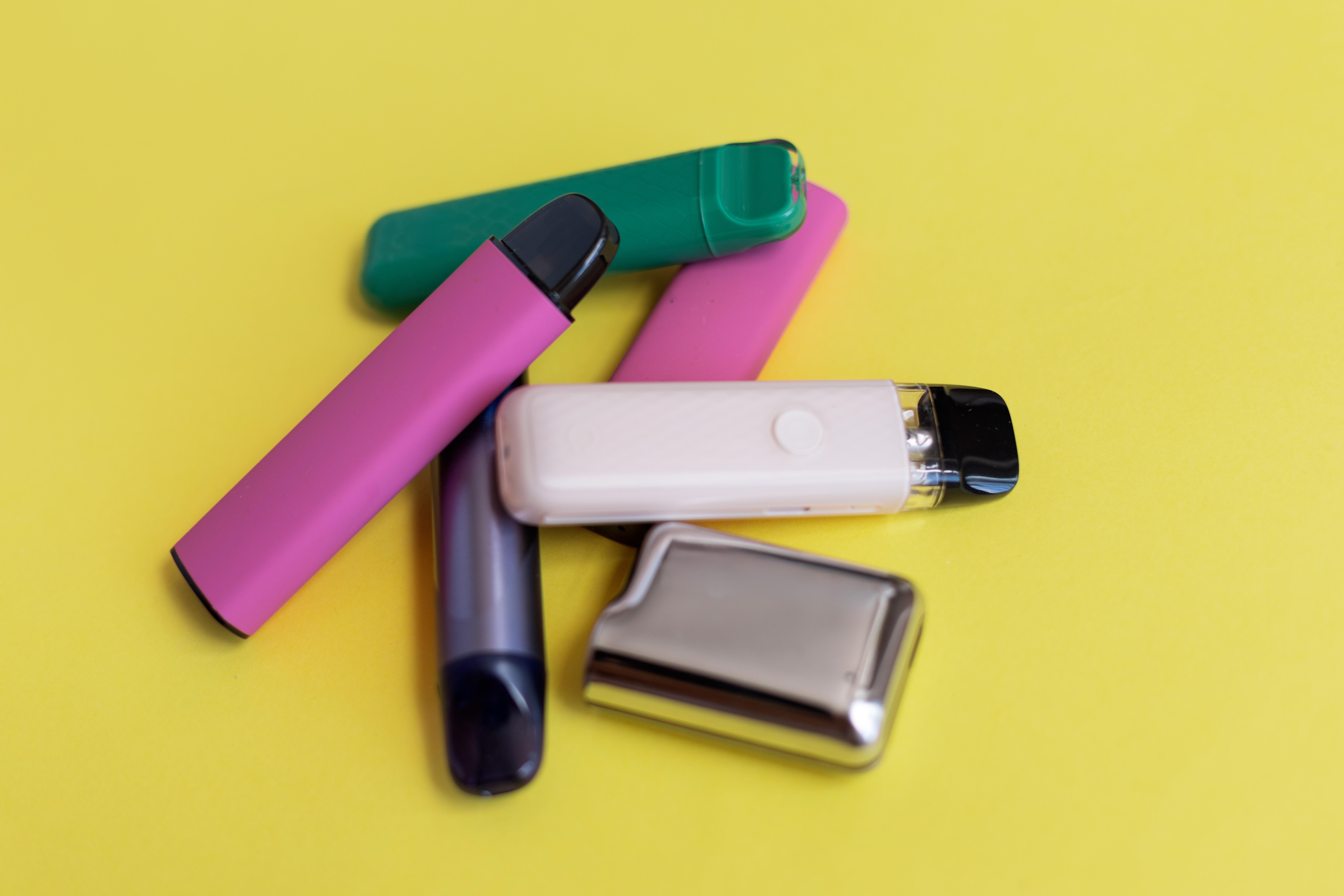 Verschiedene Vaping-Geräte liegen auf einem gelben Hintergrund.