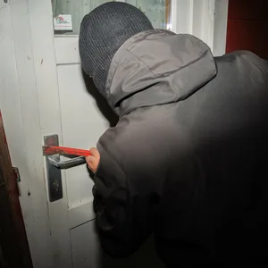 Ein vermummter Mann versucht mit einem Brecheisen eine Haustür aufzubrechen.