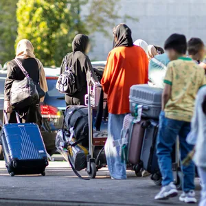 Menschen aus Afghanistan laufen mit ihrem Gepäck aus einem Flughafengebäude.