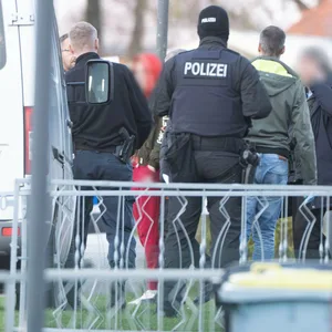 Eine tatverdächtige Frau (Mitte l.) verlässt in Begleitung von Polizeibeamten ihr Wohnhaus.