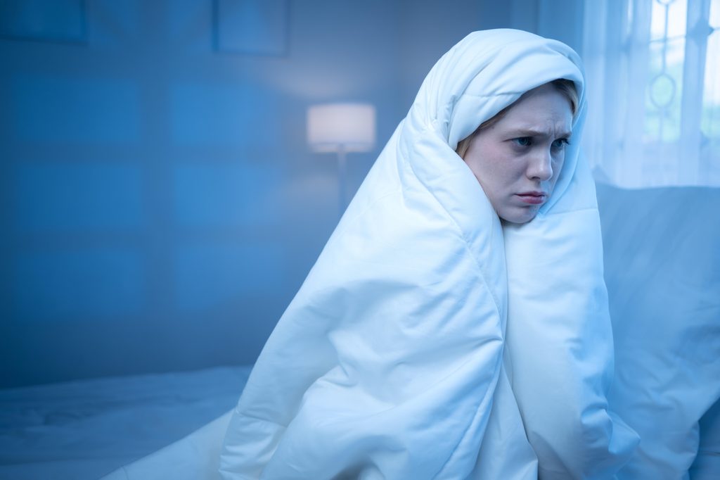 Eine Frau sitzt in eine Decke eingewickelt auf einem Bett.