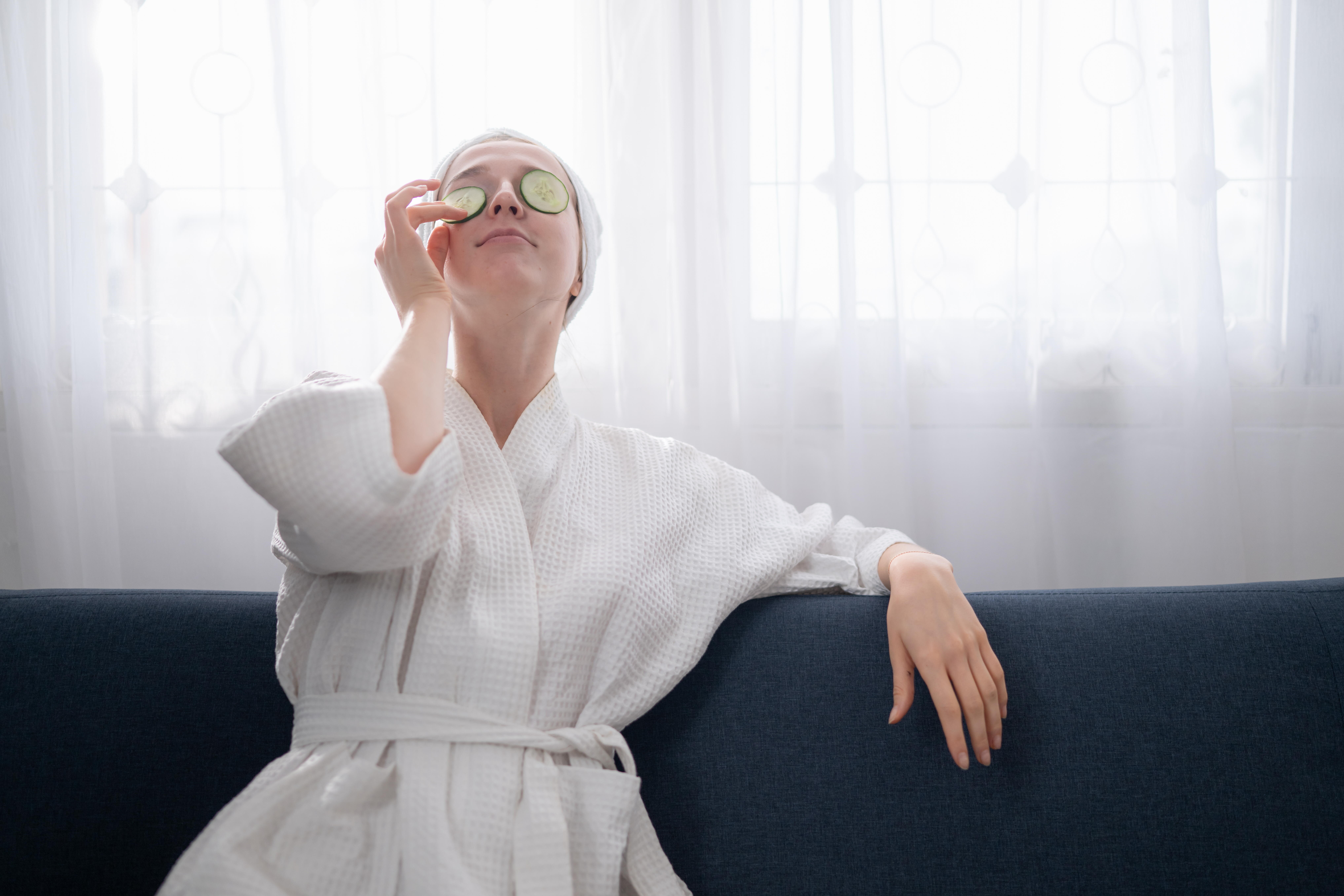 Eine Frau im Bademantel legt sich Gurkenscheiben auf die Augen