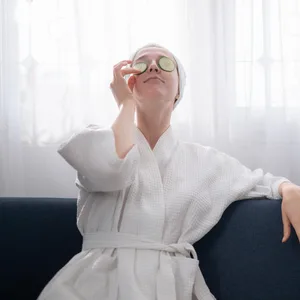 Eine Frau im Bademantel legt sich Gurkenscheiben auf die Augen
