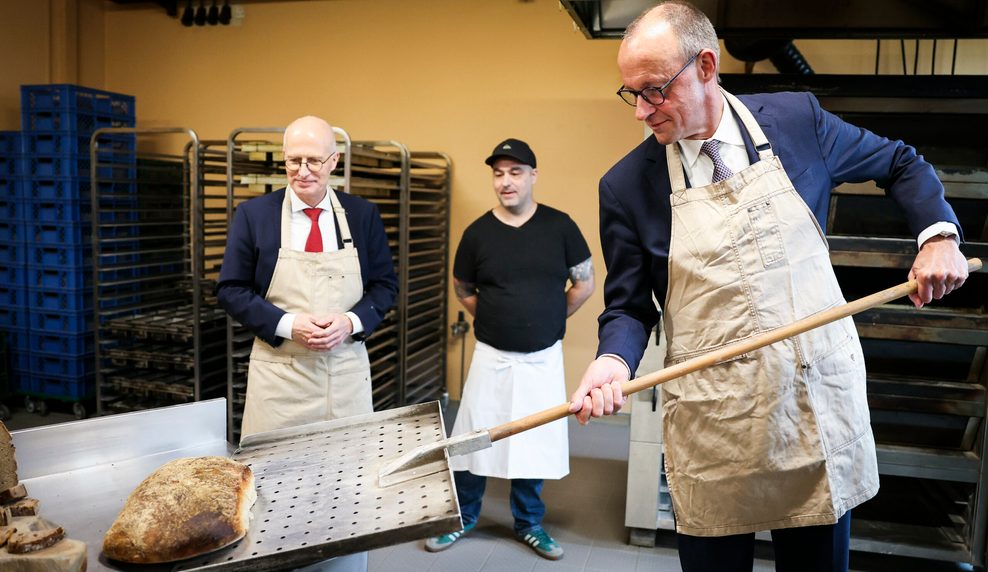 Bundeskanzler Friedrich Merz (CDU, r) und Peter Tschentscher (SPD, l), Erster Bürgermeister von Hamburg, holen in der Backstube der Brotmanufaktur von Sören Korte (M) Brot aus dem Ofen bei einem Besuch auf dem Handwerkerhof Meistermeile.