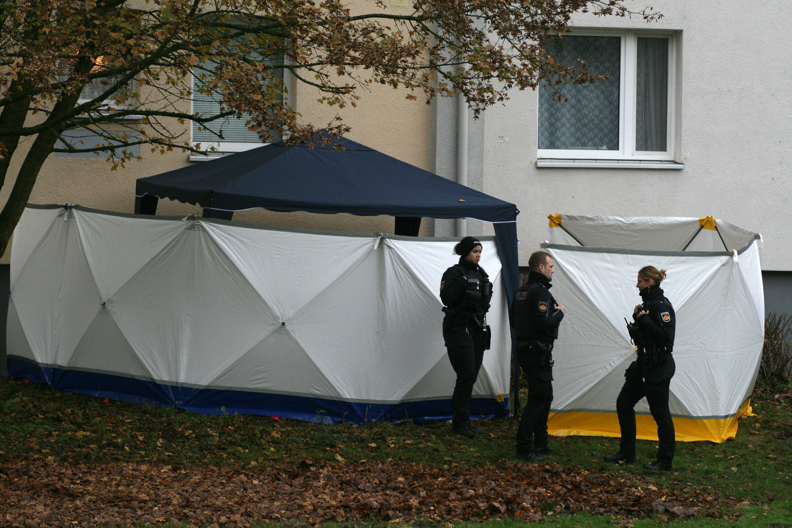 Polizisten stehen vor einem Wohnhaus an einer mit Sichtschutz versehenen Unglücksstelle.