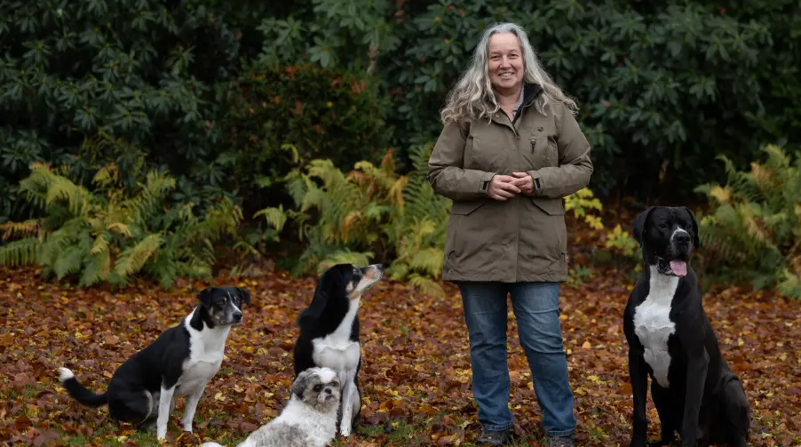 Tierpsychologin Nicole Nowak steht zwischen vier Hunden. Im Hintergrund sind Büsche und Bäume zu sehen.