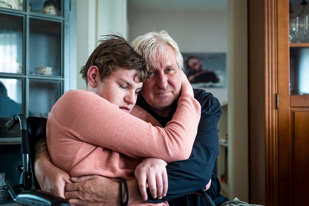 Ein Mann umarmt seinen Sohn, der im Rollstuhl sitzt.