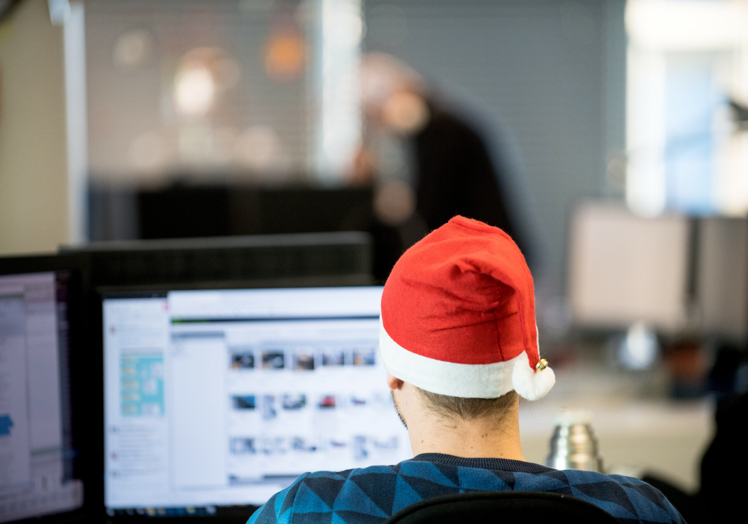 Ein Mann sitzt mit Weihnachtsmütze im Büro.
