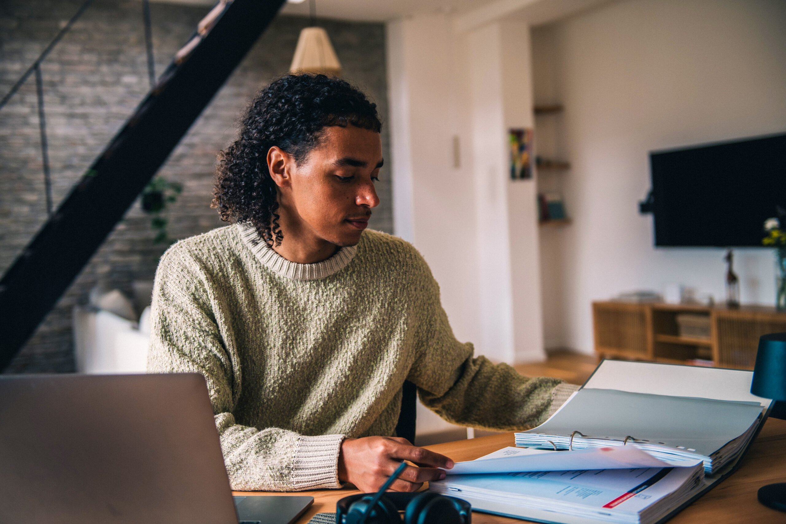 Mann sitzt vor Laptop und geöffnetem Aktenordner und prüft Unterlagen für steuerliche Aufgaben zum Jahresende 2025.
