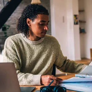 Mann sitzt vor Laptop und geöffnetem Aktenordner und prüft Unterlagen für steuerliche Aufgaben zum Jahresende 2025.