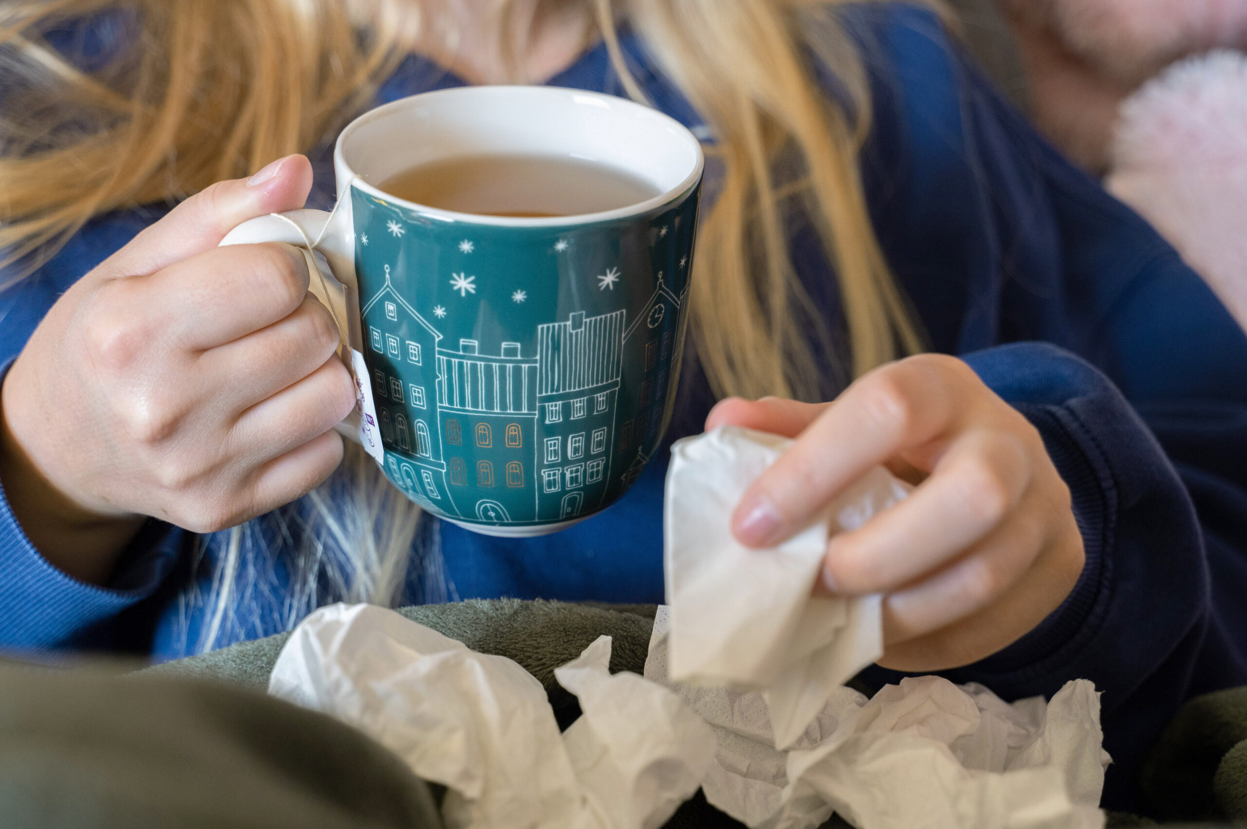 Eine Frau trinkt Tee und hält ein Taschentuch in ihrer Hand.