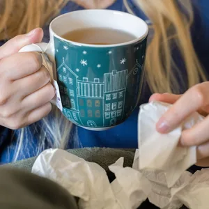 Eine Frau trinkt Tee und hält ein Taschentuch in ihrer Hand.