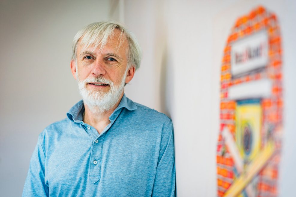 Geschäftsführer des „Hinz&Kunzt“-Magazins Jörn Sturm steht in hellblauem Hemd gegen eine Wand gelehnt.