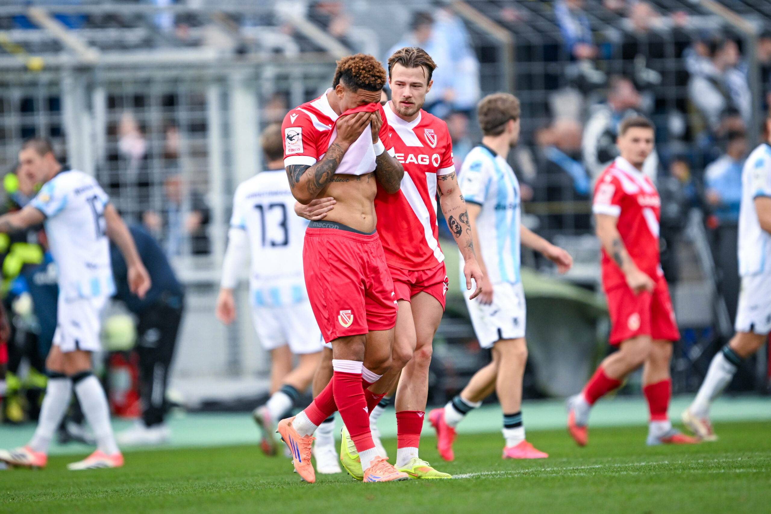 Justin Butler (l.), der sich sein Trikot vors Gesicht hält, um seine Tränen zu verdecken, wird von seinem Teamkollegen Henry Rorig (r.) getröstet