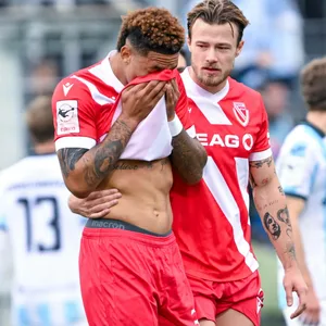 Justin Butler (l.), der sich sein Trikot vors Gesicht hält, um seine Tränen zu verdecken, wird von seinem Teamkollegen Henry Rorig (r.) getröstet