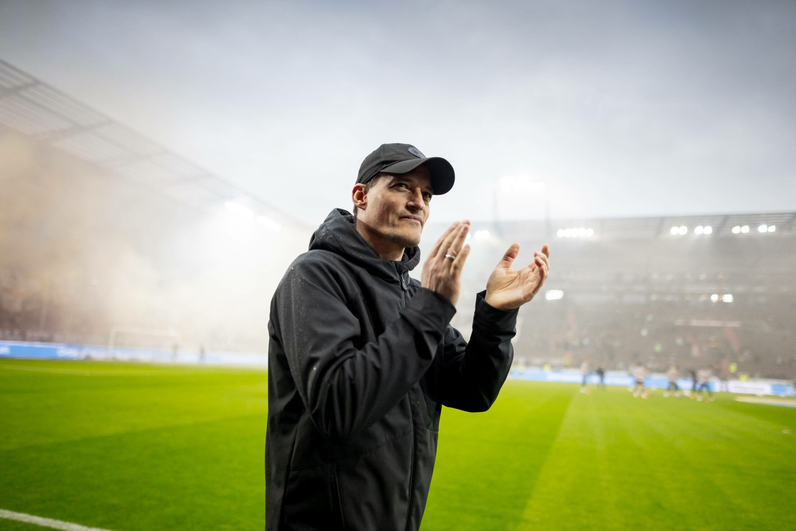 Alexander Blessin applaudiert, hinter ihm füllen Rauchschwaden das Millerntor.