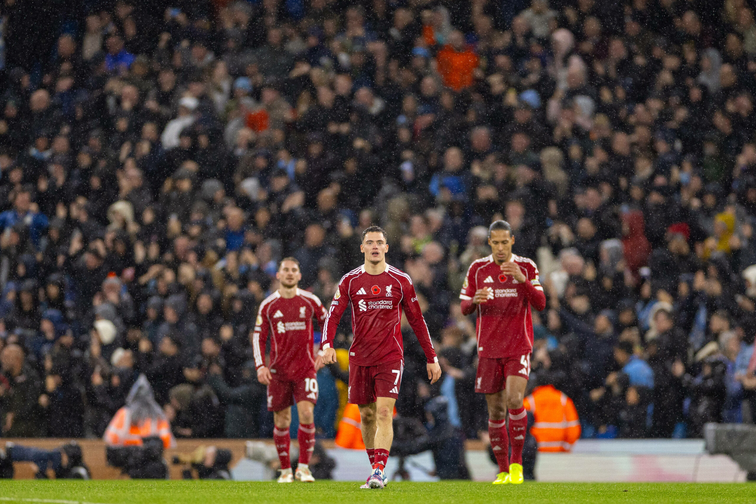 Alexis Mac Allister (l.), Florian Wirtz (m.) und Virgil van Dijk (r.) vom FC Liverpool, stehen bedient im Regen von Manchester