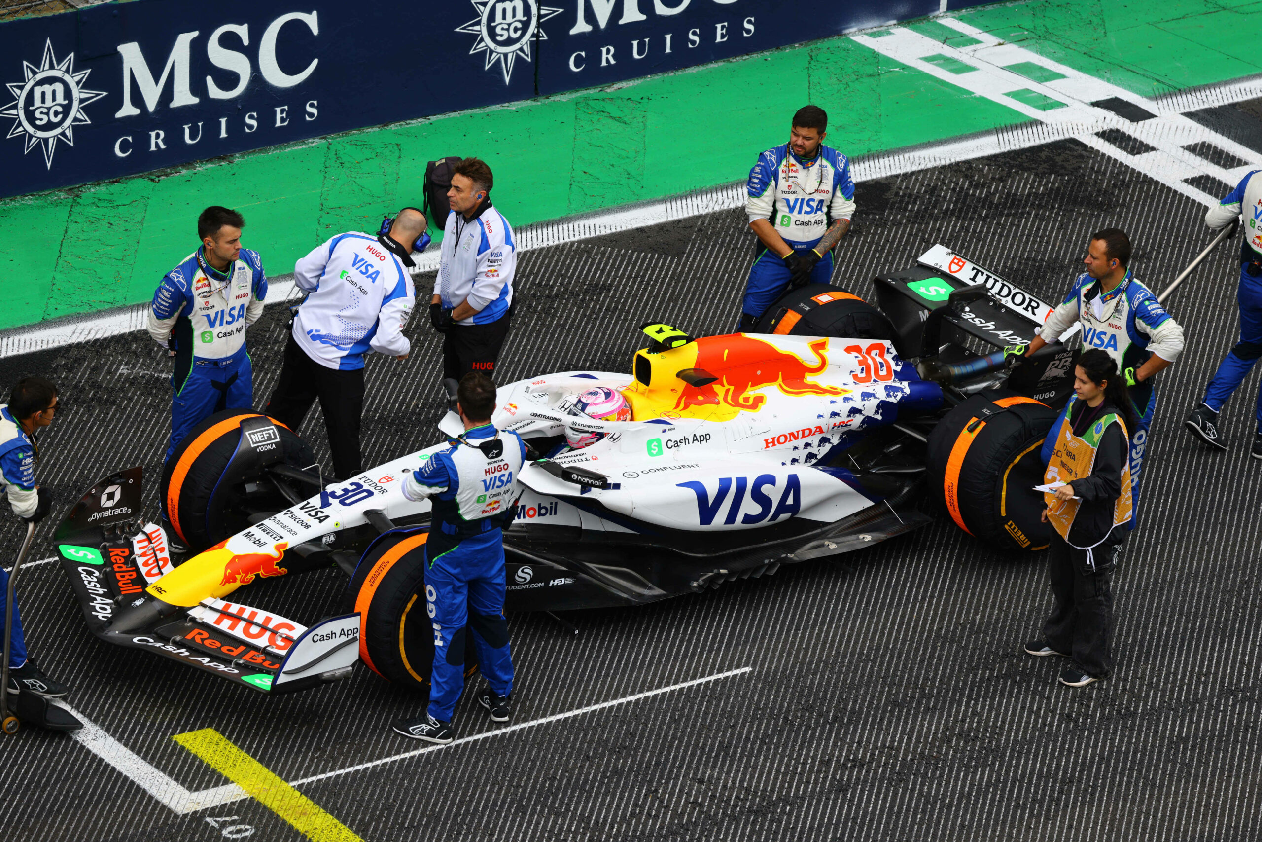 Mitarbeiter des Formel-1-Teams Racing Bulls stehen neben dem Auto, von Racing Bull Fahrer Liam Lawson, in der Startposition