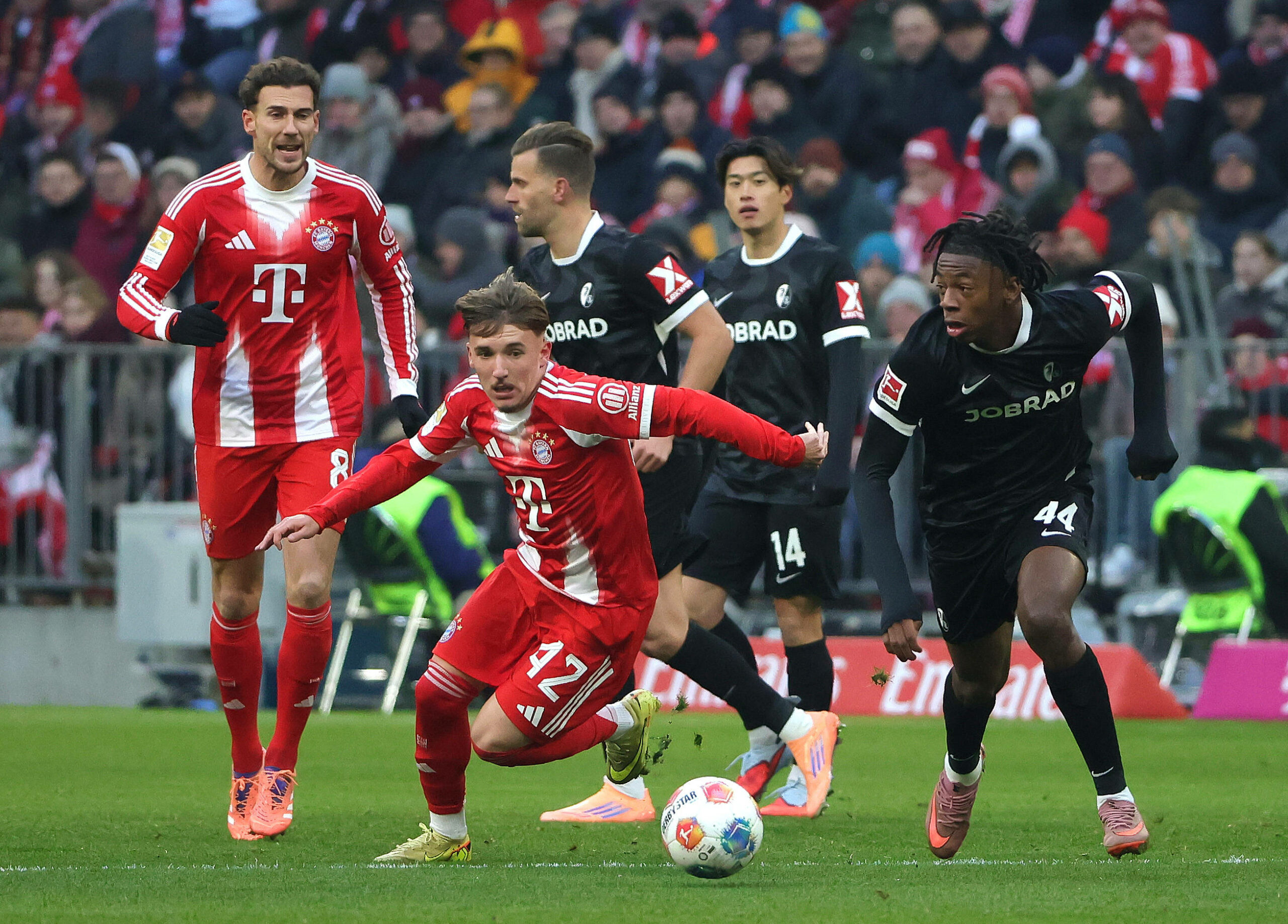Lennart Karl (FC Bayern München; 2 v. l.) dribbelt Johan Manzambi (SC Freiburg, r.) aus