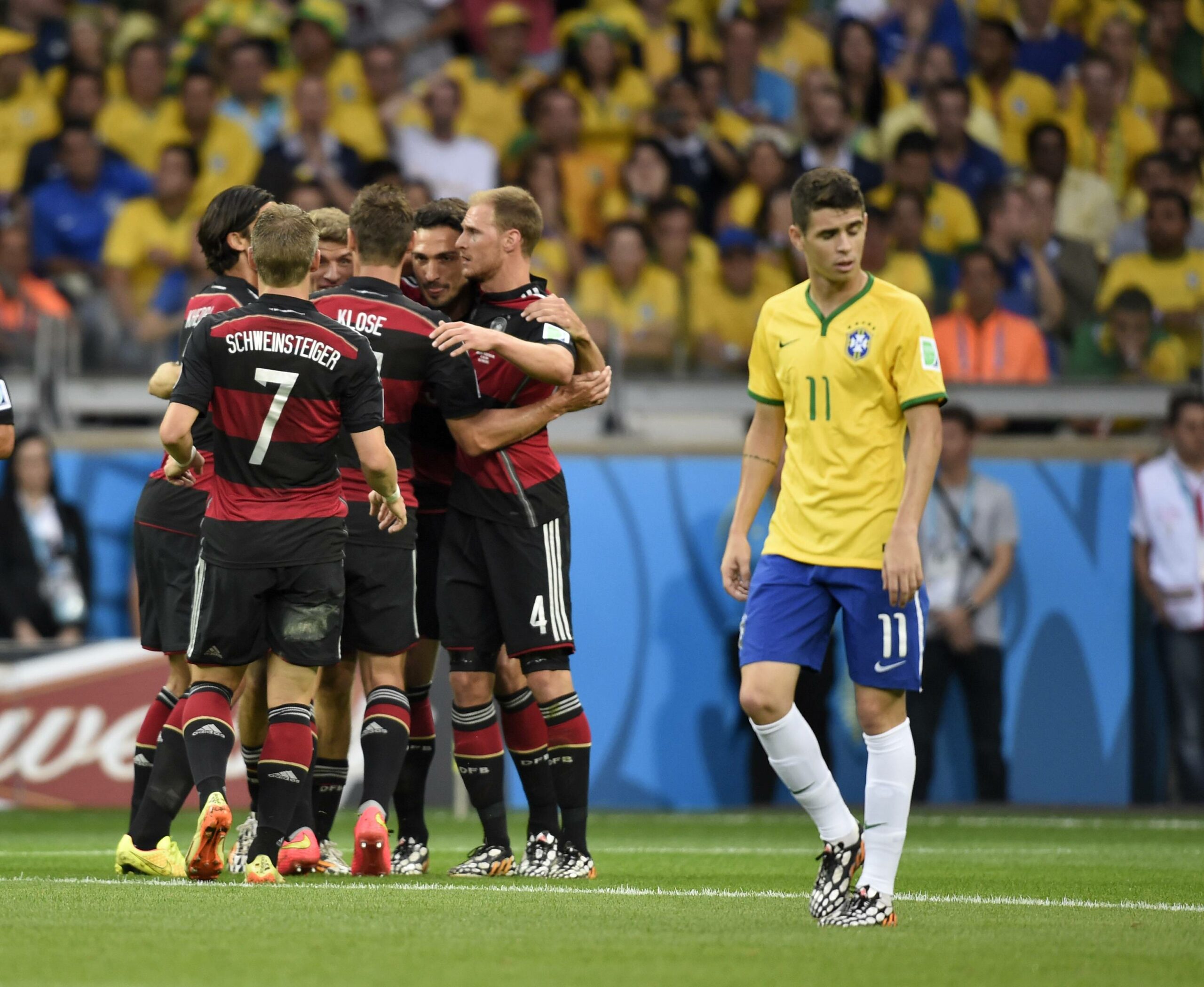 Brasiliens Oscar trabt übers Feld, während die DFB-Elf im Hintergrund jubelt.