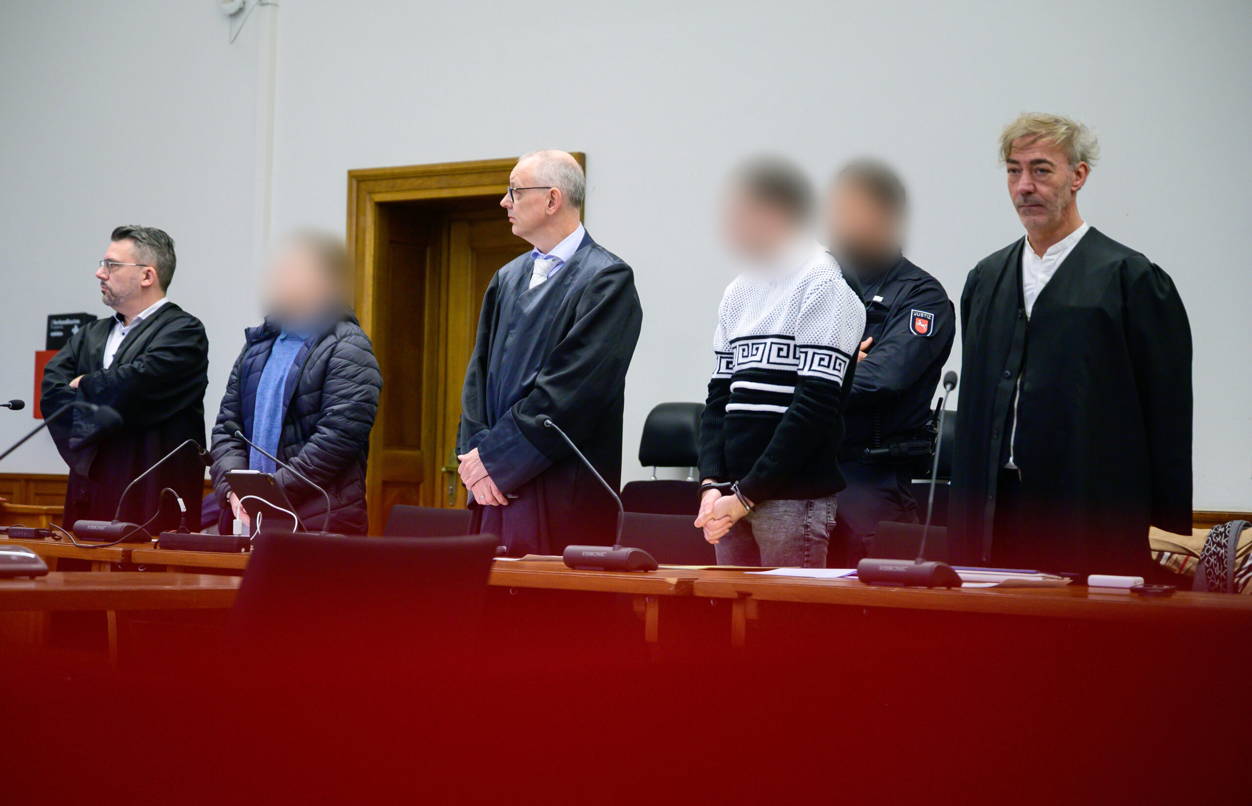 Die beiden Angeklagten (2.v.l und 3.v.r) stehen beim Auftakt im Prozess wegen versuchten Mordes neben ihren Anwälten im Gerichtssaal des Landgerichts Lüneburg.