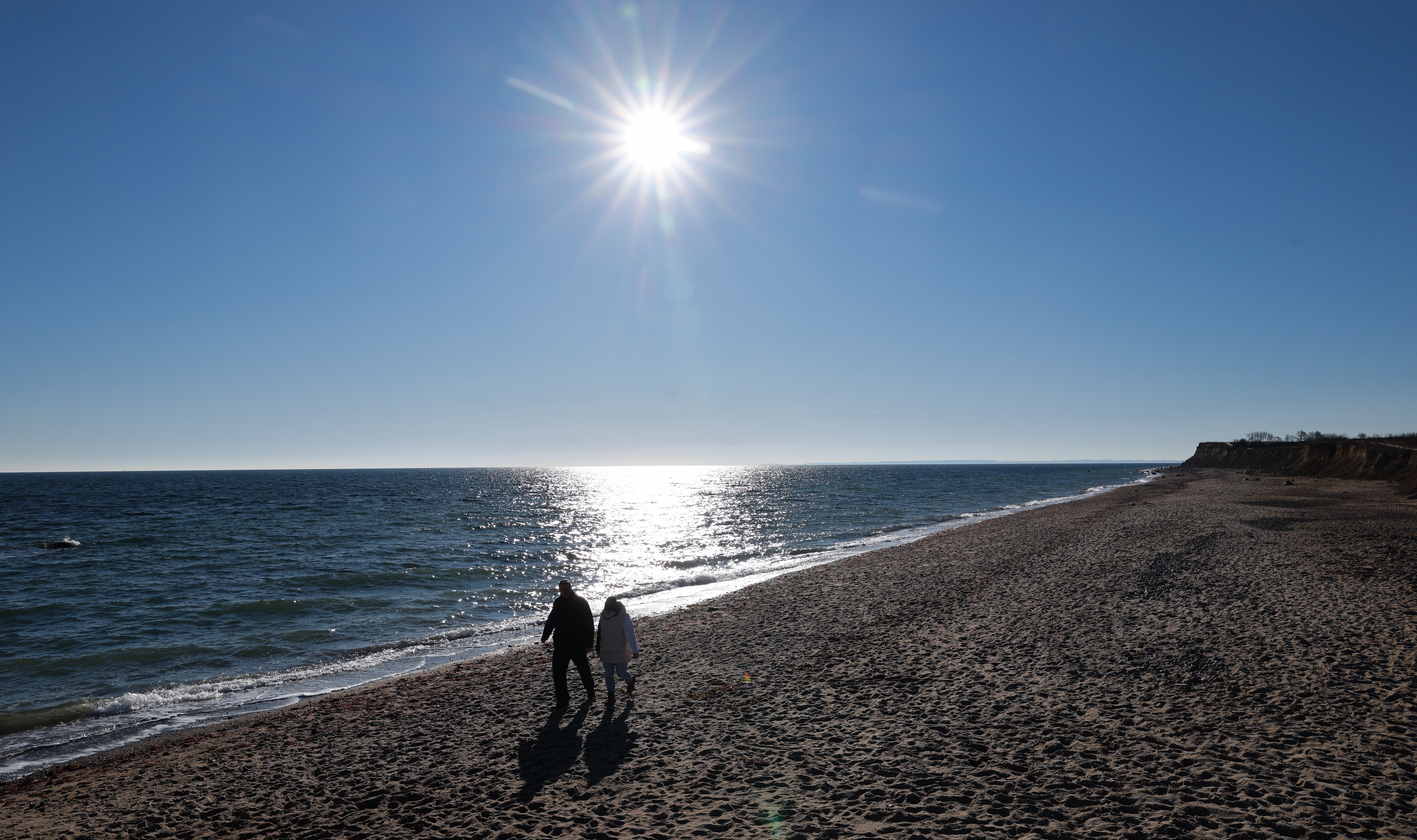 Menschen sind bei strahlendem Sonnenschein und frostigen Temperaturen an der Schönhagener Steilküste an der Ostsee unterwegs.