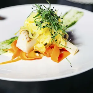 Elegantes Meeresfrüchtefilet, serviert mit Juliennegemüse, Microgreens und Kräutersauce auf einem weißen Gourmetteller.