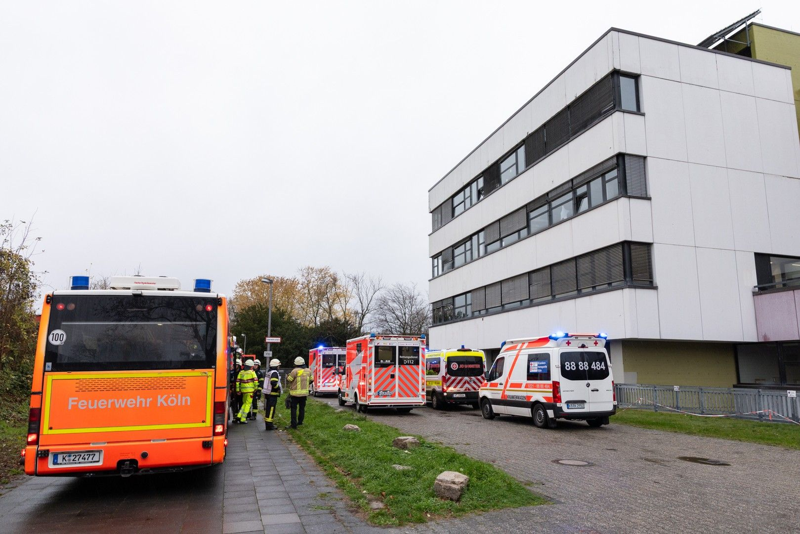 Einsatzkräfte der Feuerwehr stehen vor einer Schule.
