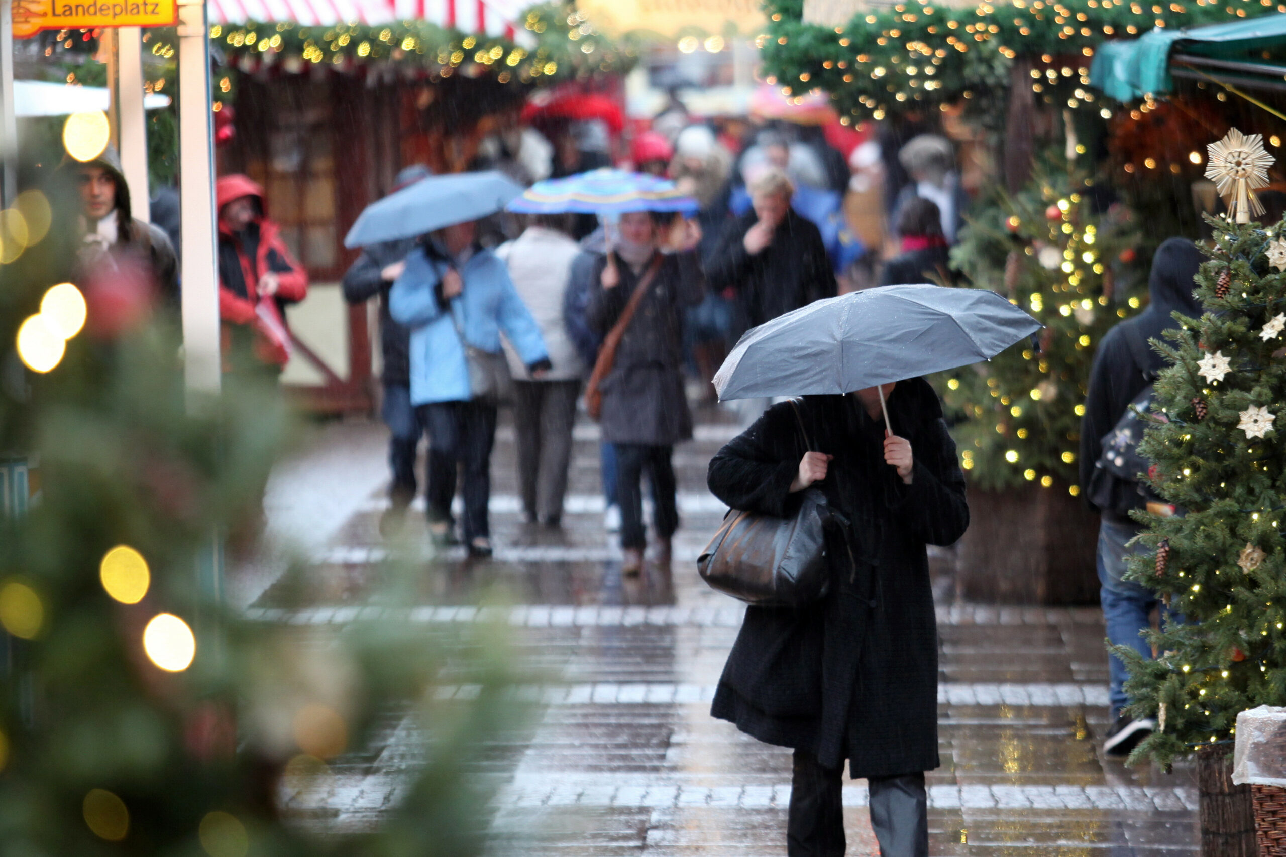 Mit Regenschirmen schützen sich Passanten auf einem Weihnachtsmarkt.