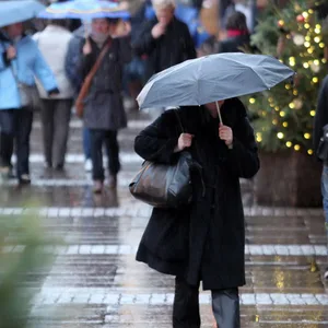Mit Regenschirmen schützen sich Passanten auf einem Weihnachtsmarkt.