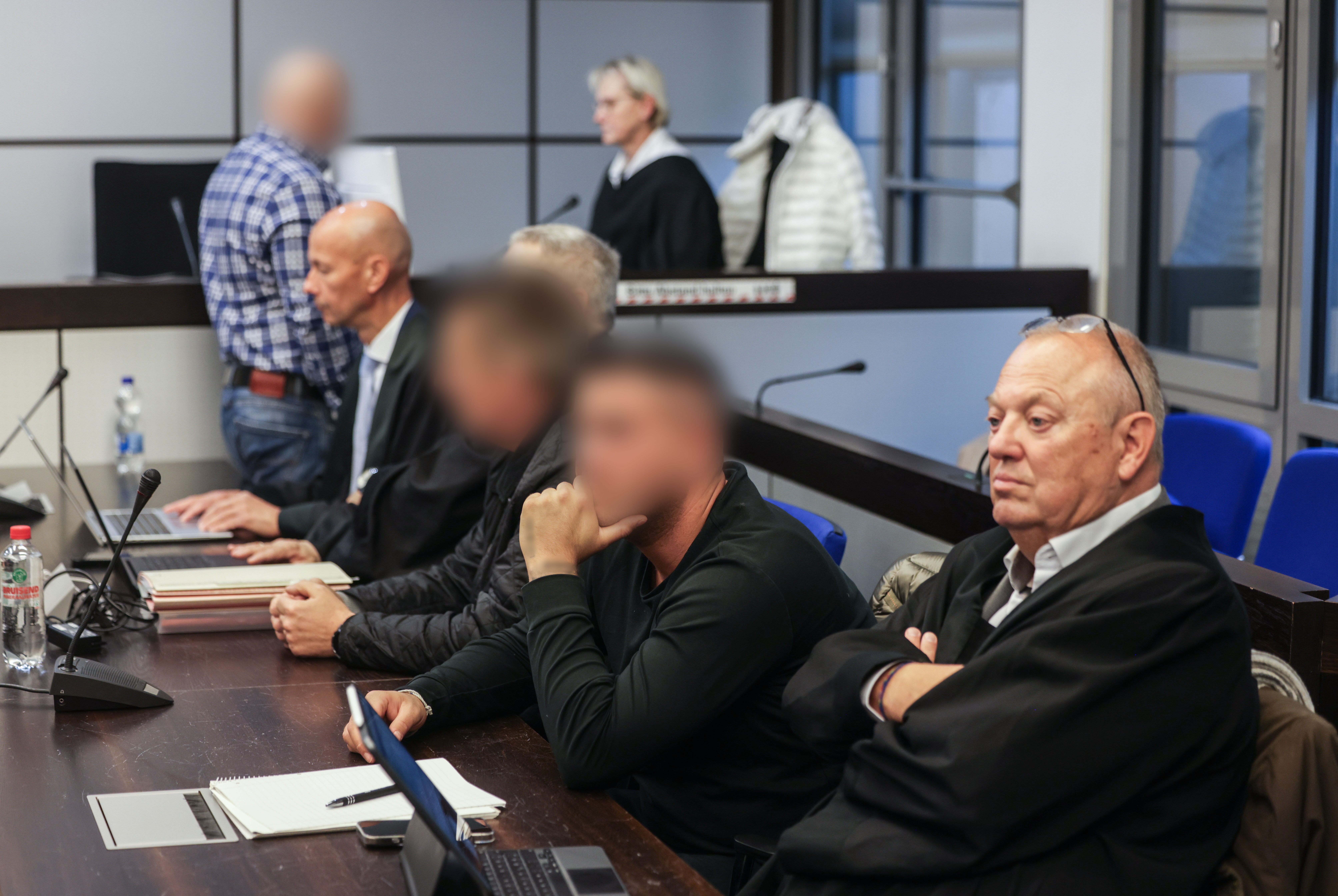 Die drei Angeklagten (hinten l., 2.v.r. und 3.v.r) sitzen zwischen ihren Anwälten im Landgericht Wuppertal.